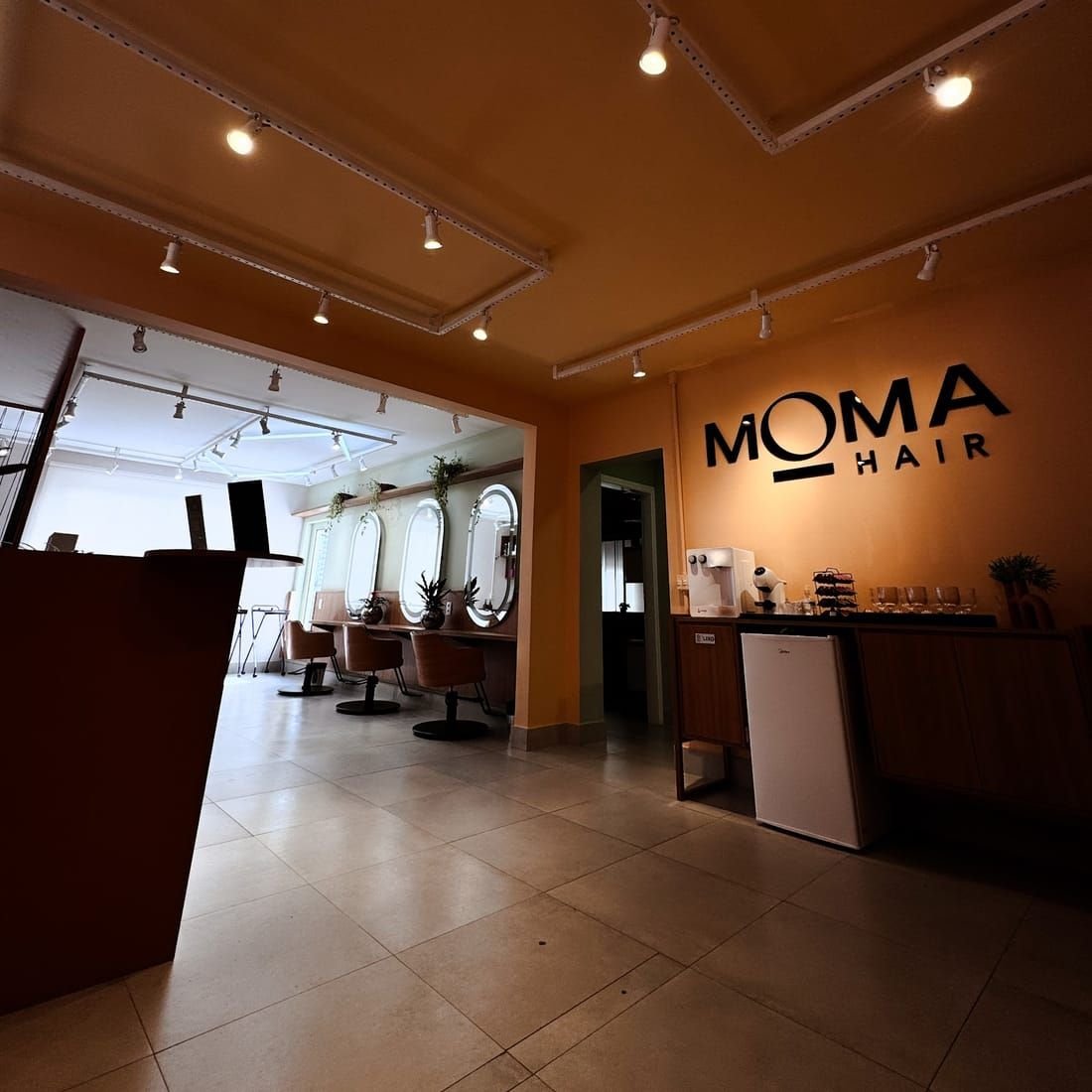 Recepção do Moma Hair com parede laranja e letreiro da marca